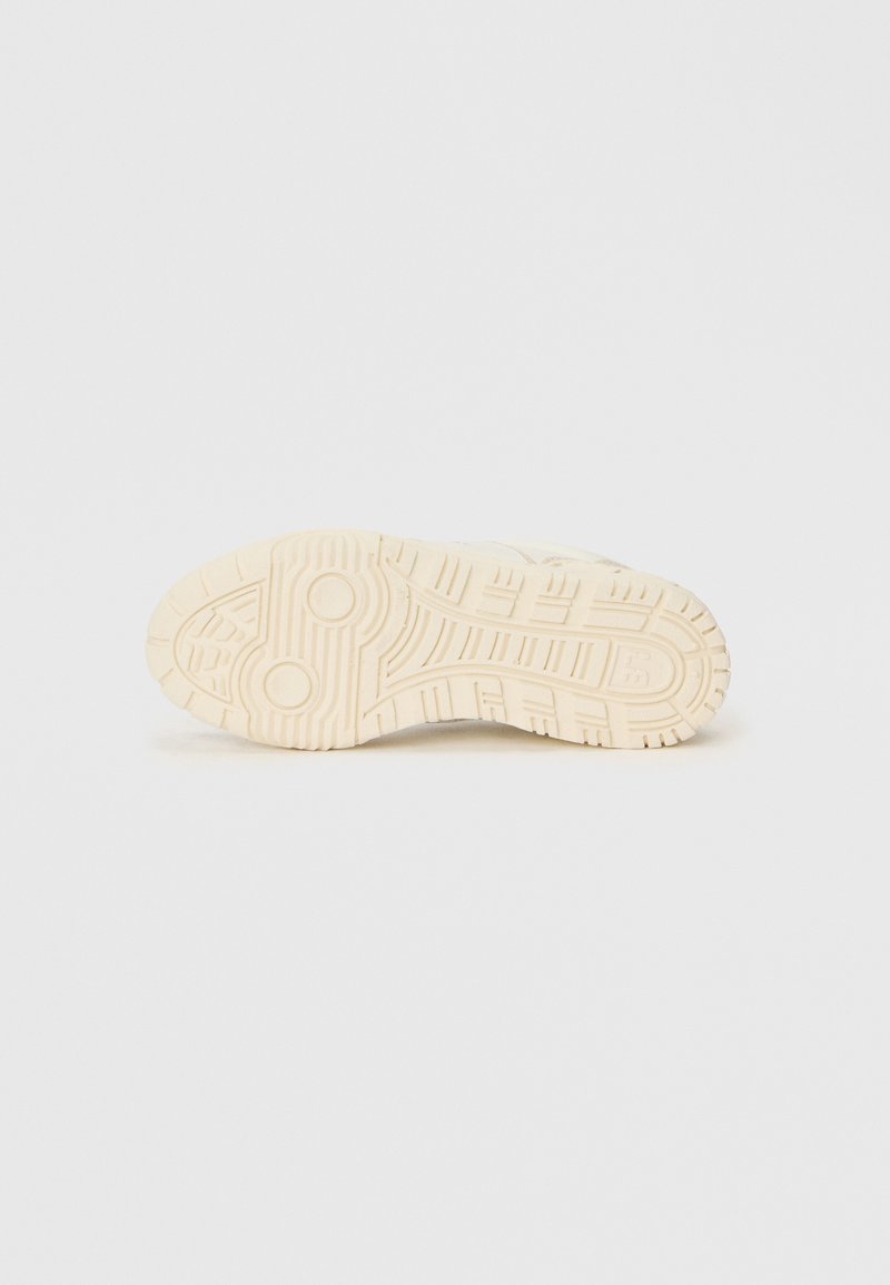 Suela de zapatilla en goma blanca. Presenta un patrón de relieve texturizado con diseños circulares y lineales para un mejor agarre. Superficie suave alrededor de la banda de rodadura.