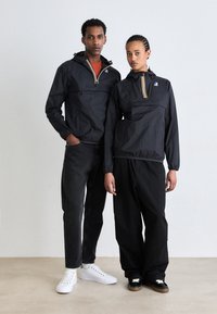 Zwarte lichtgewicht jassen met rits aan de voorkant, voorzien van kleurrijke strepen, gecombineerd met zwart-witte sneakers en een comfortabele broek.