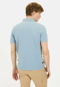 Lichtblauwe polo met korte mouwen, voorzien van een klassieke kraag en zijsplitten. Gemaakt van gladde stof. Gecombineerd met kaki cargoshorts.