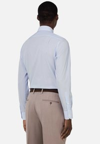 Camicia azzurro chiaro a maniche lunghe con colletto strutturato; indossata con pantaloni beige dotati di tasca posteriore e dettaglio con bottone.
