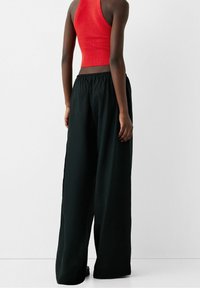 Top corto a coste rosso abbinato a pantaloni larghi neri. I pantaloni hanno un elastico in vita e una vestibilità ampia, mostrando una texture morbida.