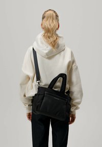 Bolso de hombro negro acolchado con dos asas y correa ajustable, que presenta una textura suave y un diseño minimalista.