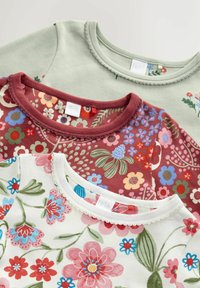 Trys medvilniniai marškiniai: šviesiai žalia, tamsiai raudona su gėlių raštu ir kreminė su spalvingomis gėlėmis. Kiekvienas turi apvalų iškirpimą ir dekoratyvinį apdailą.