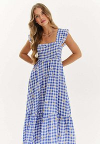Modrá a biela kostkovaná šaty so štvorcovým výstrihom, nadýchanými rukávmi, smockovaným telom a viacvrstvovou sukňou so starostlivo umiestnenými kvetinovými akcentmi.