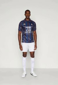 Jalgpallijersey tumesinise kangaga, punaste vertikaalsete triipudega ja valge logo/tekstiga. Sobitatud valgete lühikeste pükste ja põlvepikkuste valgete sokkidega.