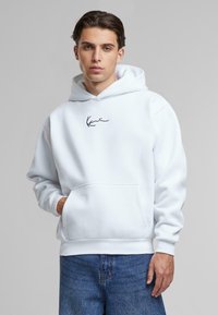 Hoodie blanc avec poche kangourou et poignets côtelés. Présente un logo noir en signature sur la poitrine. Tissu en mélange de coton doux.