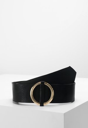 Ceinture en cuir noir avec une large sangle et une grande boucle ronde dorée posée sur une surface blanche.