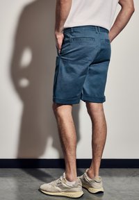 Modré bavlněné šortky s ohrnutými manžetami, které mají hladký povrch a boční kapsy. Spárované s krémovými teniskami s semišovými detaily.