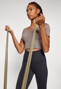 Beige cropped ribbed top met korte mouwen, gecombineerd met hoge zwarte leggings. Grip op elastische weerstandsbanden in beide handen.