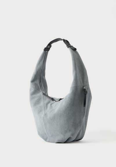 Sac à bandoulière en daim gris doux avec une forme arrondie, une sangle noire réglable et des fermetures éclair argentées visibles à l'avant et sur le côté.