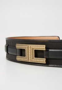 Black leather belt with a smooth texture, featuring a prominent gold geometric buckle design and black leather strap.