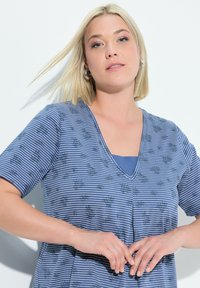 Camisa a rayas azules con mangas cortas, diseño de cuello en V, patrón floral y una textura suave. Lleva una camiseta interior azul por debajo.