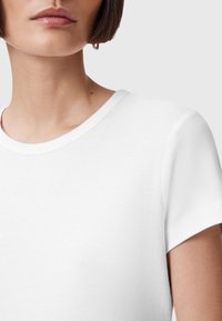 T-shirt bianca a maniche corte con scollatura rotonda, texture liscia e design minimalista, che mostra parte del collo e della spalla.