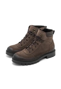 Botas de tobillo de ante marrón con acentos en marrón oscuro, puntera redonda, ojales metálicos y suela de goma negra resistente. Cuenta con un collar acolchado.