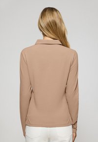 Brun långärmad skjorta med krage i en slät textur, med sidslitsar vid fållen. Skjortan har en figursydd design och en avslappnad look.