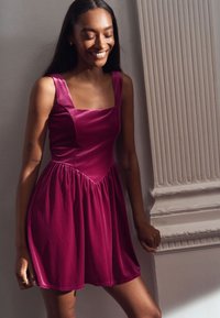 Fuchsia Samtkleid mit quadratischem Ausschnitt, tailliertem Oberteil und gerafftem Rock. Verfügt über dünne Träger und eine glatte Textur.