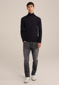 Maglione a collo alto navy in tessuto morbido, abbinato a jeans grigi e sneakers bianche. Design semplice, silhouette aderente e dettagli a coste.