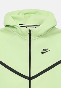 Svetlozelená zipová mikina s čiernymi akcentmi, so stojatým golierom a logom Nike na ľavej strane. Mäkka textúra látky.