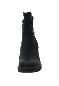 Botte chelsea en cuir noir avec une texture lisse, fermeture éclair sur le côté et une sangle autour de la cheville ornée d'une boucle en argent. Semelle en caoutchouc plate.