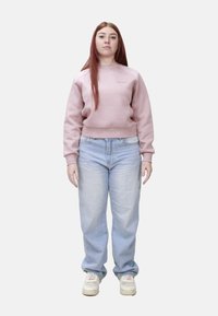 Felpa corta rosa chiaro con polsini a coste, abbinata a jeans a vita alta azzurri e sneakers bianche. Outfit semplice e casual.