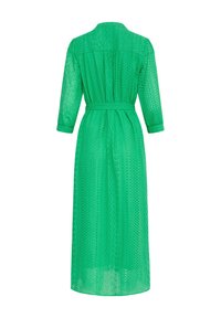 Vestito verde in pizzo con maniche a tre quarti, una vita con cintura e motivi traforati ovunque. Il design presenta una schiena aderente e una silhouette fluida.