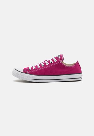 Low-Top Sneaker aus magentafarbenem Canvas mit weißer Gummikappe, weißen Schnürsenkeln und weißer Sohle mit schwarzen Streifen vor weißem Hintergrund.