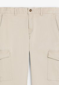 Pantaloni cargo bej, fabricați dintr-un material rezistent. Au un închidere cu nasture, două buzunare laterale și două buzunare mari pentru depozitare.