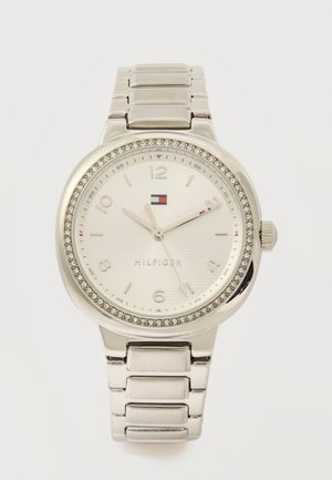 Silver Tommy Hilfiger wristwatch with crystal-studded bezel, metallic band, and white dial showing 10:10:55 time.
