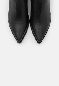 Černé kožené kotníkové boty s špičatou špičkou, hladkým povrchem a minimalistickým designem. Elegantně zakřivený podpatek pro dodatečnou eleganci.