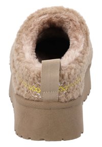 Zapatilla beige con parte superior de textil suave, cuello acolchado, tira de agarre y suela de goma con acabado texturizado. Detalles de costura amarilla.