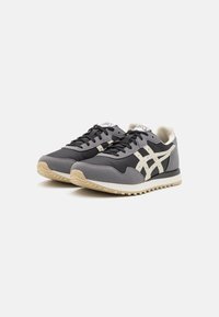 Gray athletic sneakers with a textile upper, suede accents, white branding, and a cream rubber sole. Features a lace-up design.