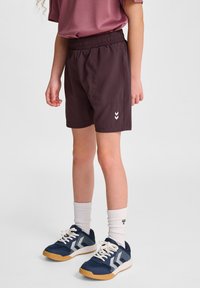 Mörklila shorts med elastisk midja, kombinerat med marinblå sneakers och vita ribbade strumpor. Har en vit chevronlogotyp på shorts.