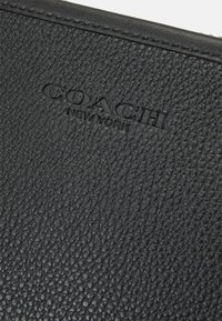 Black leather wallet featuring a textured surface with visible grain. Embossed "COACH NEW YORK" logo at the center.