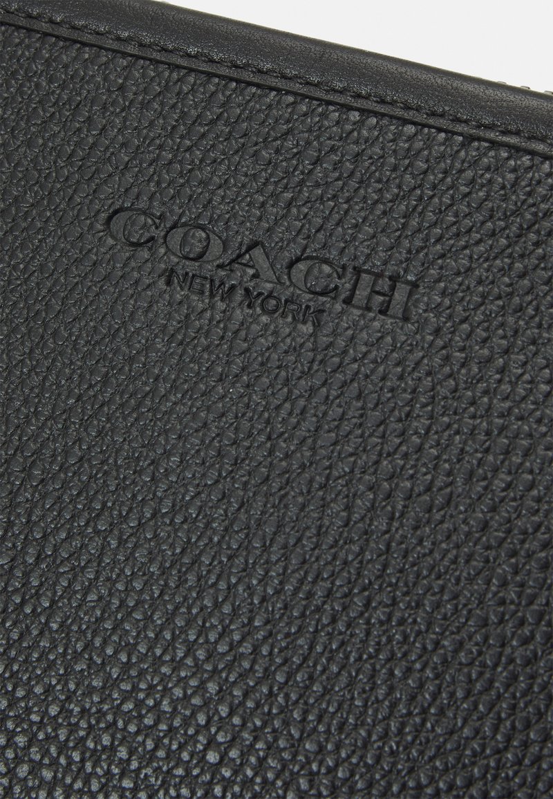 Portefeuille en cuir noir avec une surface texturée présentant un grain visible. Logo en relief "COACH NEW YORK" au centre.