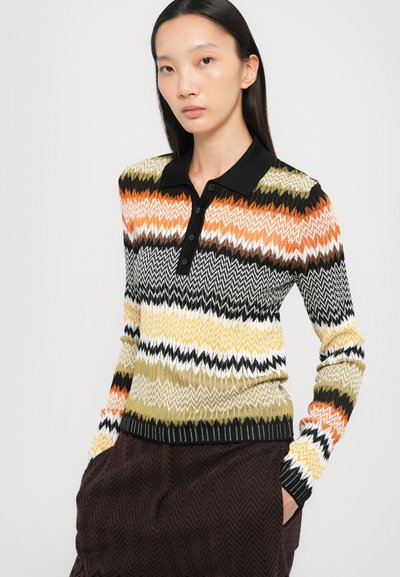 Maglione polo lavorato a maglia con motivo zigzag multicolore in arancione, nero, bianco e giallo. Presenta un colletto nero e una pattina con bottoni.
