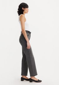 Aukštai juosmens, plačių kojų pilkos džinsus, pagamintus iš denimo, derinant su balta marškinėliais ir juodais plokščiais bateliais, matoma iš šono.