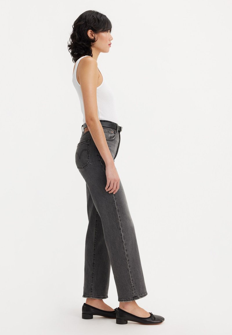 Jean gris taille haute et large en denim, associé à un débardeur blanc et des chaussures plates noires, vu de côté.