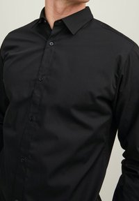 Camicia nera con bottoni in tessuto liscio, caratterizzata da un colletto alla francese e design aderente, con bottoni neri lungo il davanti.
