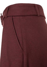 Bordeauxfarbene, maßgeschneiderte Hosen mit strukturiertem Bund, seitlichen Taschen und texturiertem Stoff für zusätzlichen Wärme- und Tragekomfort.