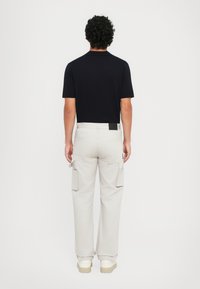Zwarte korte mouwen shirt met een kraag, gecombineerd met lichtbeige cargobroek met zijzakken en een eenvoudige zwarte label op de tailleband.