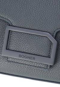 Borsa a tracolla in pelle testurizzata blu scuro con un accento in metallo grigio rettangolare etichettato "BOGNER" ricamato sulla superficie.