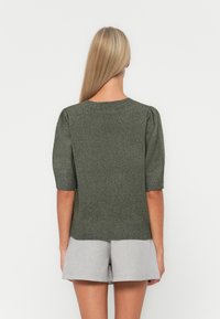 Pull en tricot vert avec des manches courtes bouffantes, des poignets et un ourlet côtelés, une texture lisse et une silhouette ajustée, associé à un short gris.