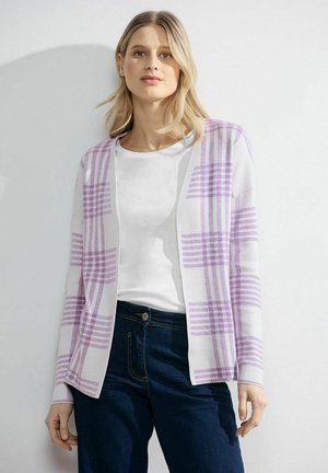 Villatakki valkoisesta kankaasta, jossa on violetti ruutukuvio, avoin etuosa, pitkät hihat, päällä valkoinen paita ja tummat farkut.