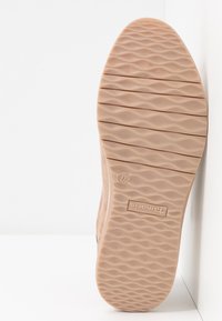 Suola di scarpa beige con motivo testurizzato e ondulato e leggera elevazione laterale. Presenta un marchio e indicatore di taglia stampati nella gomma.