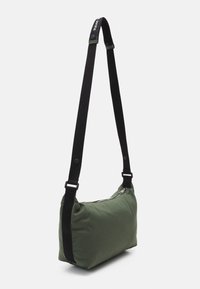 Borsa a spalla di tessuto verde con forma rettangolare, tracolla nera regolabile e chiusura lampo argentata. Texture liscia, design minimalista.