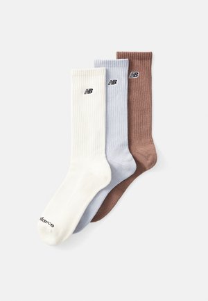 Trois paires de chaussettes en blanc, bleu clair et marron ; texture côtelée avec le logo "New Balance" en noir sur chaque chaussette.