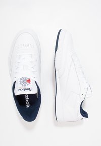 Chaussures de sport blanches en cuir texturé, avec des accents perforés et un intérieur bleu marine. Logo sur la languette et semelle en caoutchouc.