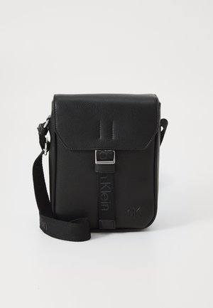 Black leather crossbody bag with a flap closure, silver hardware, adjustable strap, and embossed logo on the front. Textured surface.
