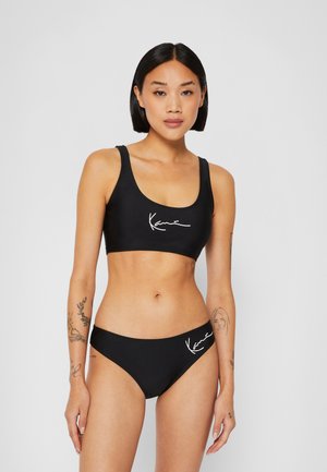 Schwarzes Bikini-Set mit einem Sportoberteil mit breiten Trägern und rundem Ausschnitt, kombiniert mit passenden tief sitzenden Unterteilen, beide mit weißen Logodetails.