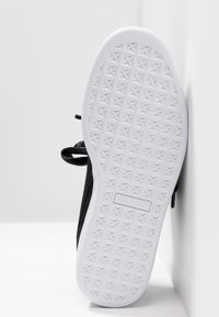 Semelle blanche texturée d'une chaussure Puma noire avec un motif en forme d'étoile en grille, présentée à la verticale sur un fond blanc en coin.